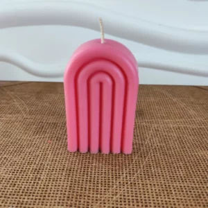 Bougie rose en forme d'arche posée sur un table en bois
