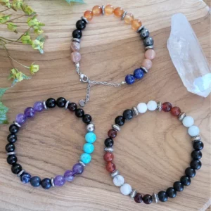 3 bracelets en pierres différentes sur du bois. Avec un cristal de roche