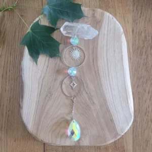 attrape solei avec deux anneaux dans lesquels se trouvent un soleil et une lune. Sur du bois avec des feuilles vertes en decoration