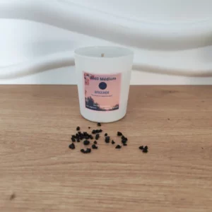 bougie dans un pot blanc et étiquette rose. incrustée de tourmaline. Plusieurs pierres tombées sur du bois. fond blanc