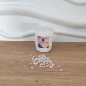 bougie en pot blanc incrustée de pierres quartz rose posée sur du bois avec fond blanc et étiquette rose