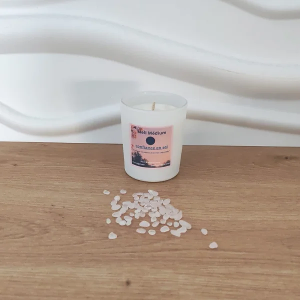 bougie en pot blanc incrustée de pierres quartz rose posée sur du bois avec fond blanc et étiquette rose