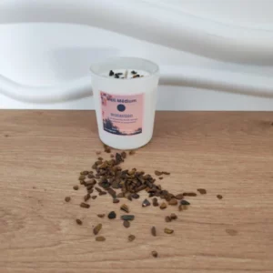 bougie en pot avec etiquette rose et pierres oeil du tigre sur du bois et fond blanc