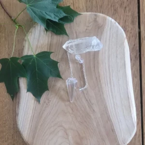 pendule en cristal de roche et chaine en acier sur du bois. Avec feuille vertes et cristal decoratif